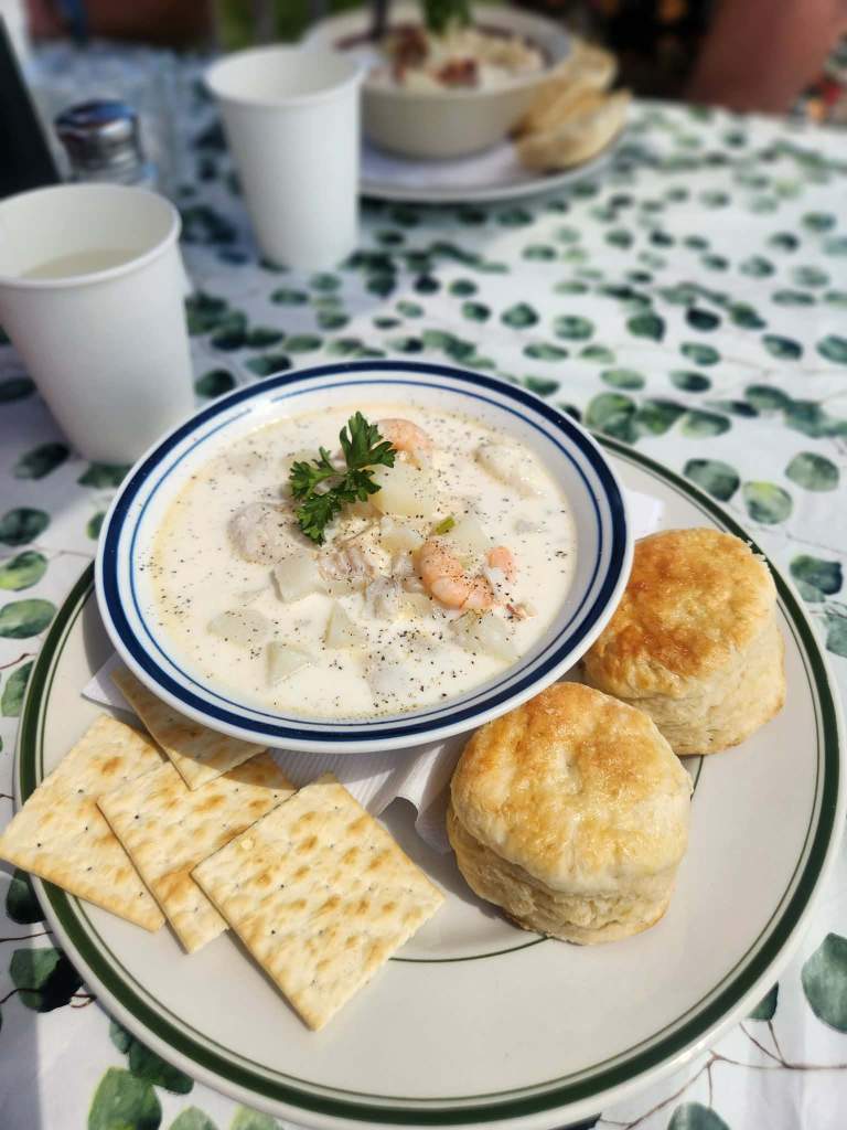 a bowl of fish chowder with biscuits and crackers at a picnic table